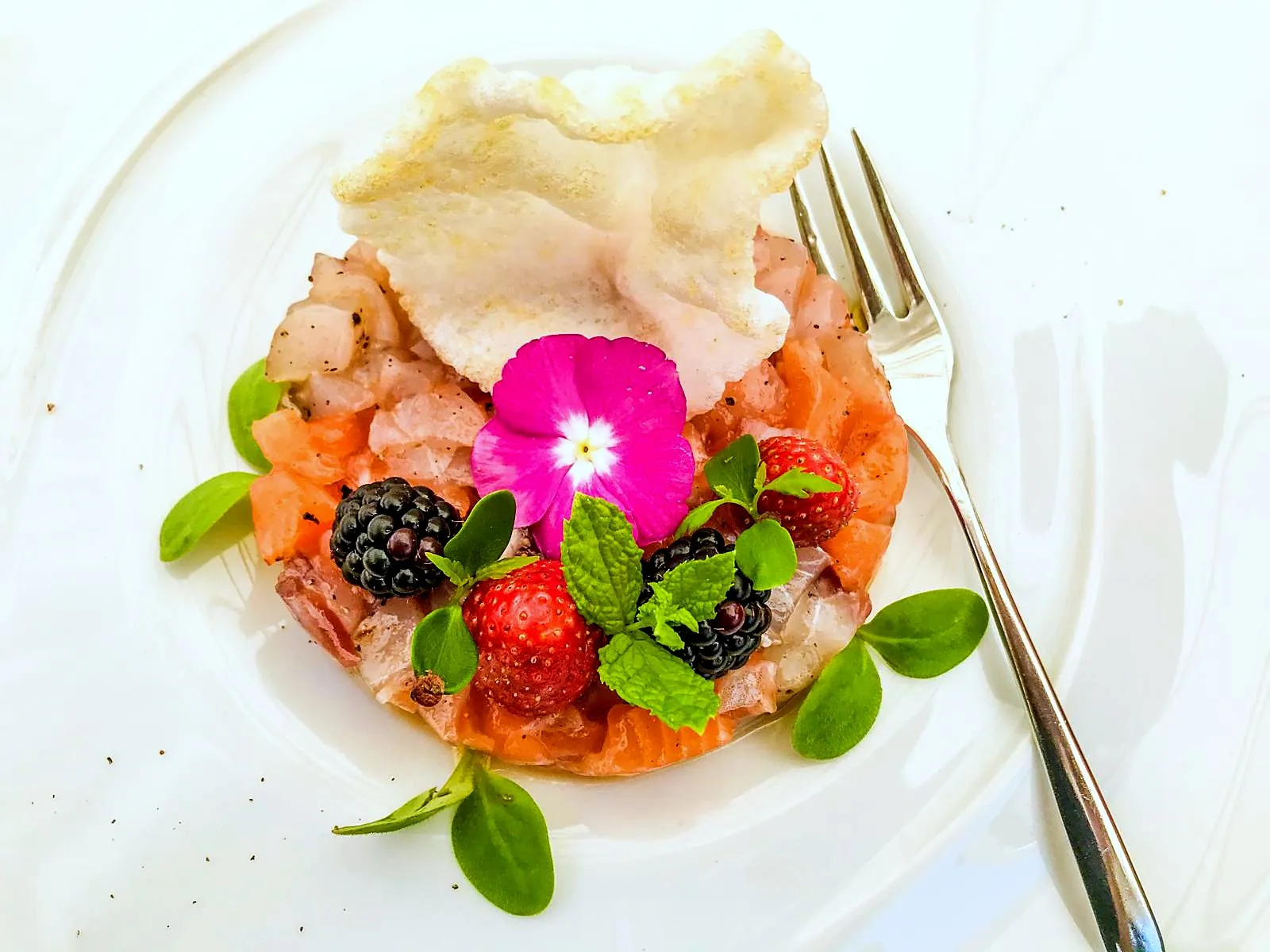 Una tartare di pesce con frutti di bosco, menta e un fiore